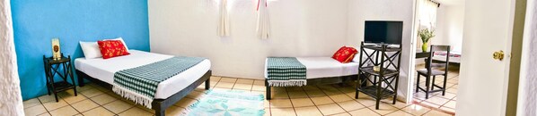 A room with two beds, a TV on a stand, a chair, and a small table. - Las Tres Palmas Hotel (Tulum)