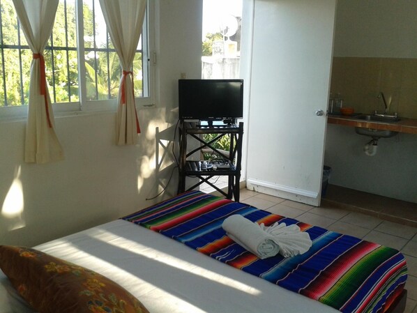 A room with a bed, a television on a stand, a small table, and a window with curtains. - Las Tres Palmas Hotel (Tulum)