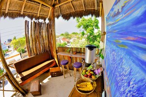 A thatched-roof outdoor seating area with a wooden bench, a table with a coffee pot, and a basket of fruits. - Las Tres Palmas Hotel (Tulum)
