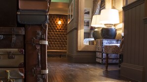 A hotel lobby with a wooden staircase, a wall-mounted lamp, and a seating area with patterned upholstery.