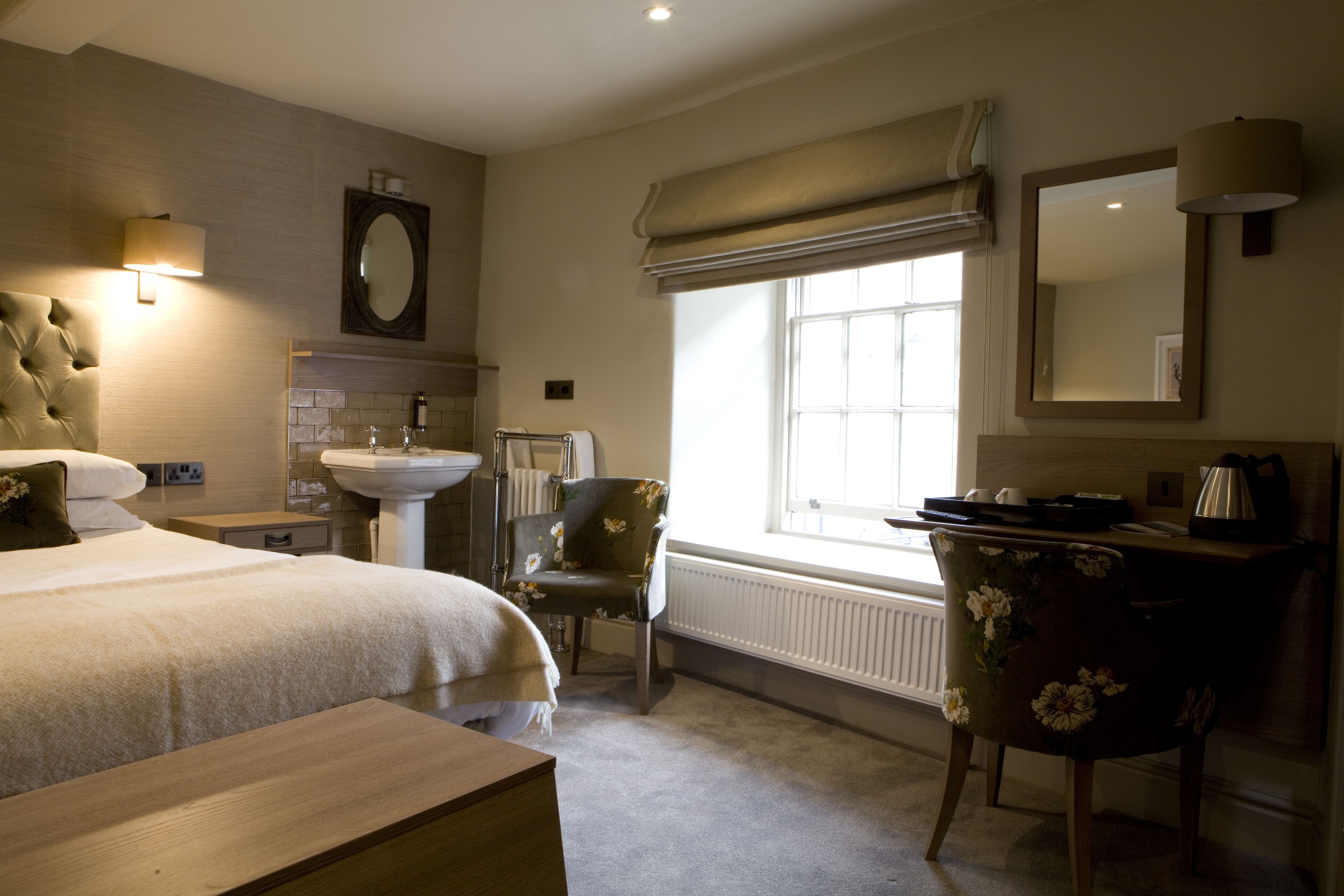 Habitación de hotel con cama, escritorio con lámpara, silla, ventana con vistas y baño con lavabo y espejo.