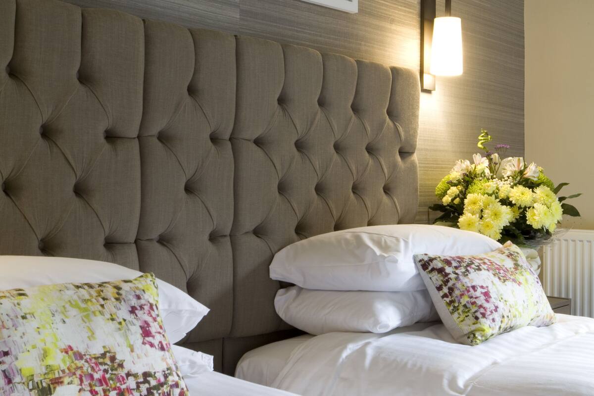 A neatly made bed with white linens and decorative pillows, a tufted headboard, and framed artwork on the wall.