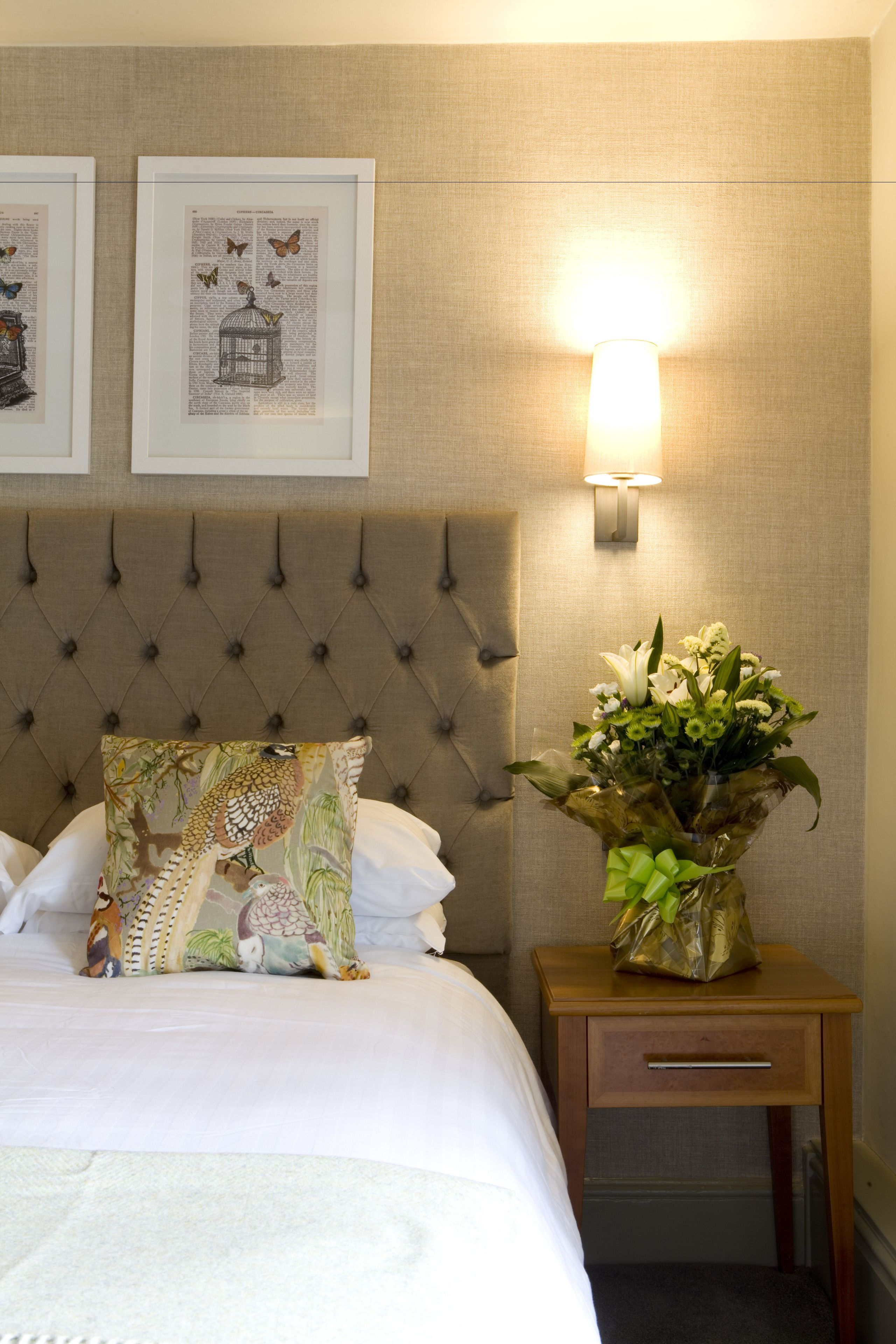 A neatly made bed with a decorative pillow, a bedside table with a vase of flowers, and framed artwork on the wall.