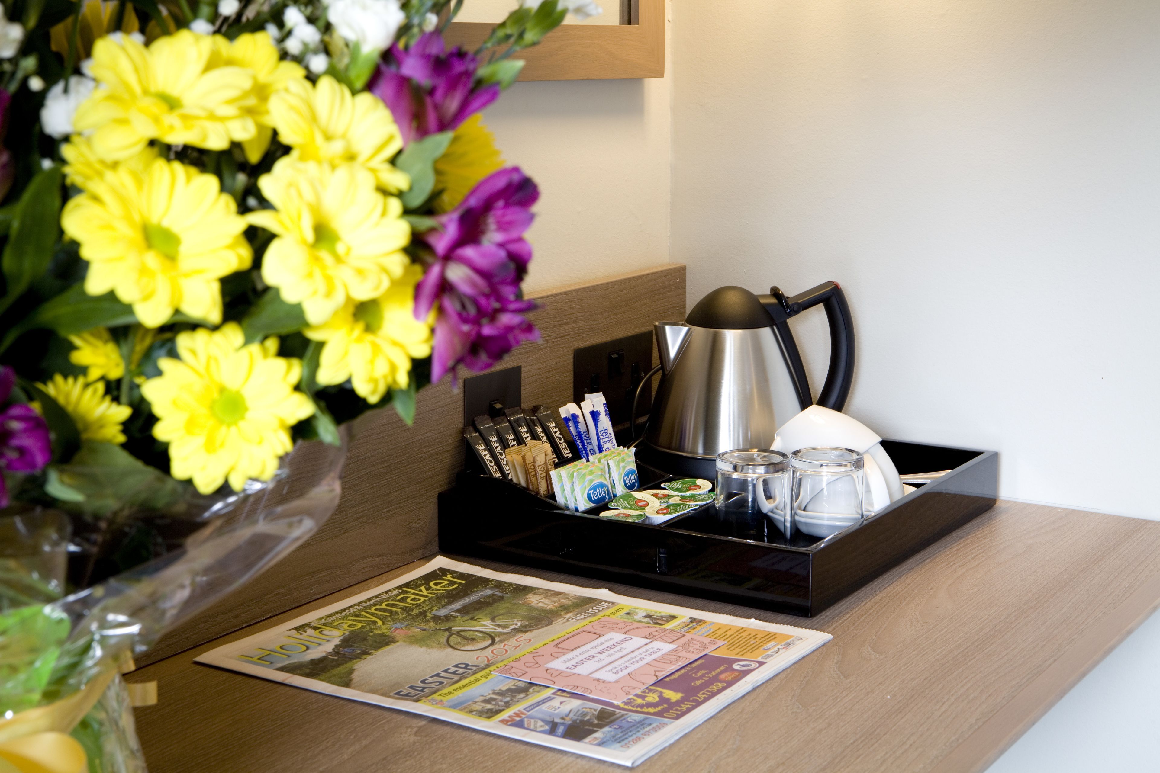 A hotel reception desk with a newspaper, a tray with coffee cups, a kettle, and a vase of flowers.