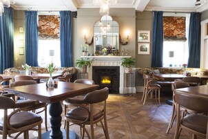 Un comedor con mesas y sillas de madera, una chimenea y cortinas azules.