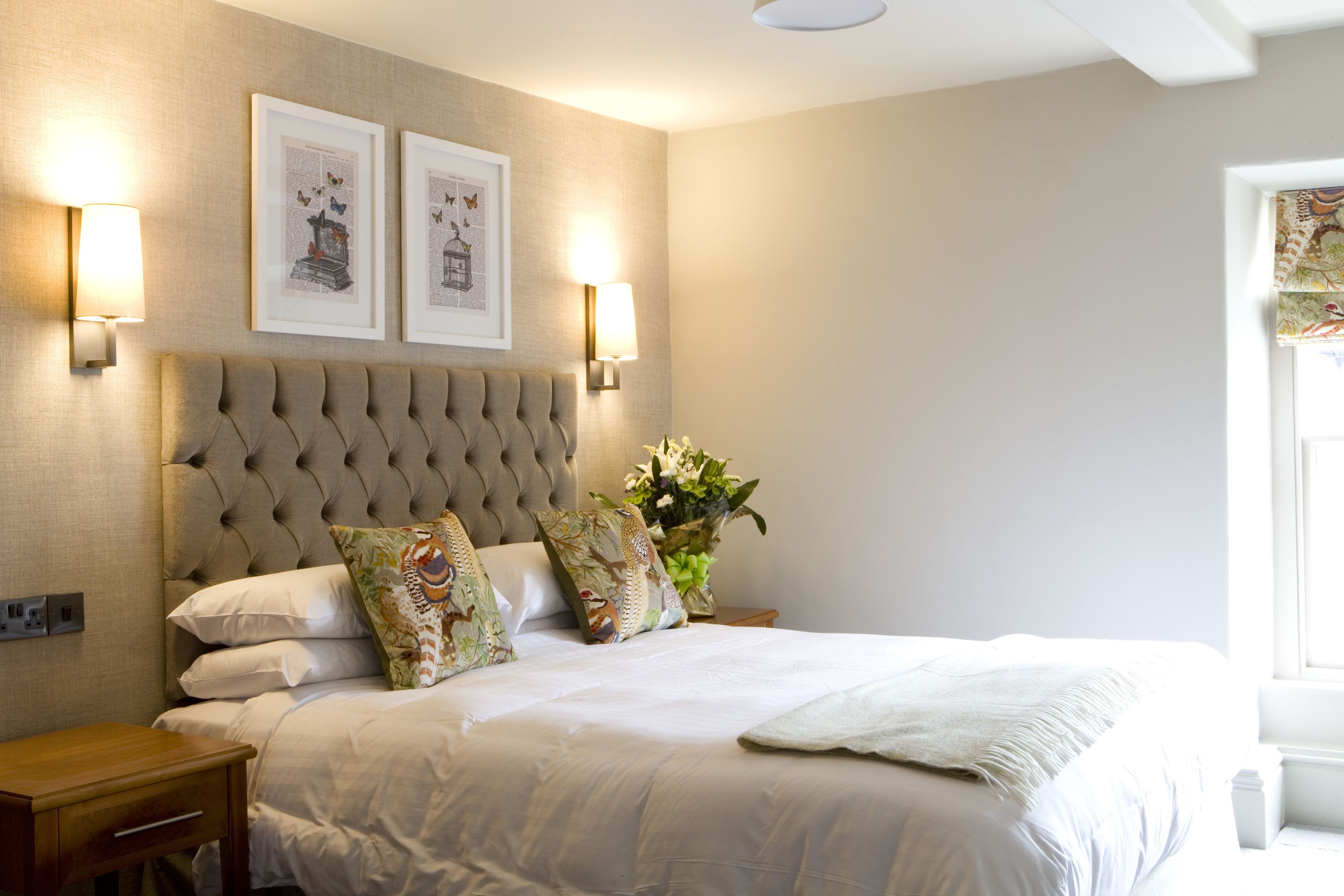 A neatly made bed with a tufted headboard, two wall-mounted lamps, and framed artwork above.
