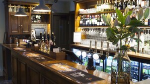 A bar area with wooden cabinets, a counter with a menu, and a variety of bottles and glasses.