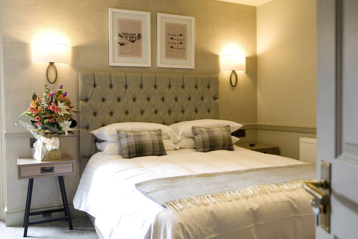 A neatly made bed with a tufted headboard, a bedside table with a lamp, and a wall-mounted picture frame.