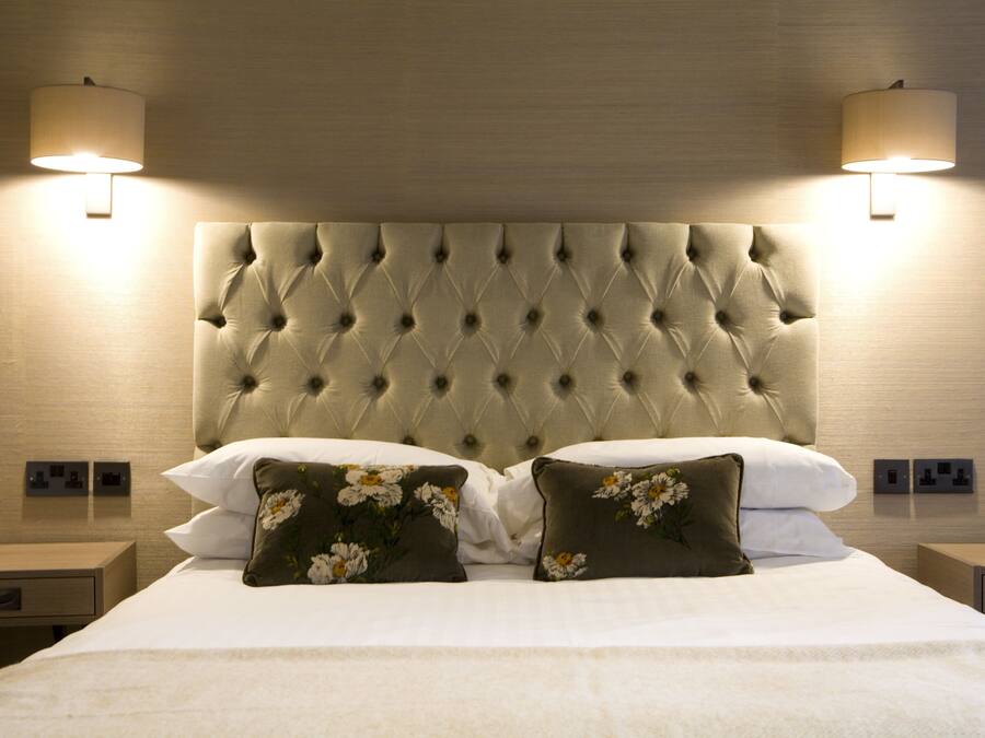 Un llit ben arropat amb un capçal tapissat, dues làmpades de nit i almoinades florals.
