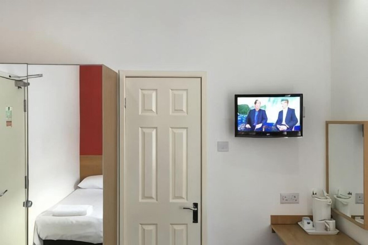 A hotel room with a bed, a television mounted on the wall, a door, and a mirror.