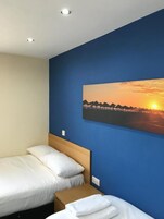 Een hotelkamer met twee bedden, een houten hoofdeinde, een nachtkastje en een schilderij van een zonsondergang aan de muur.