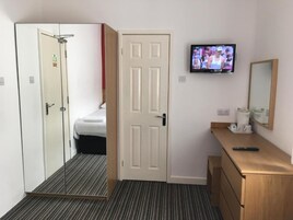 Een hotelkamer met een bed, een aan de muur bevestigde televisie, een houten dressoir en een deur die naar een andere kamer leidt.
