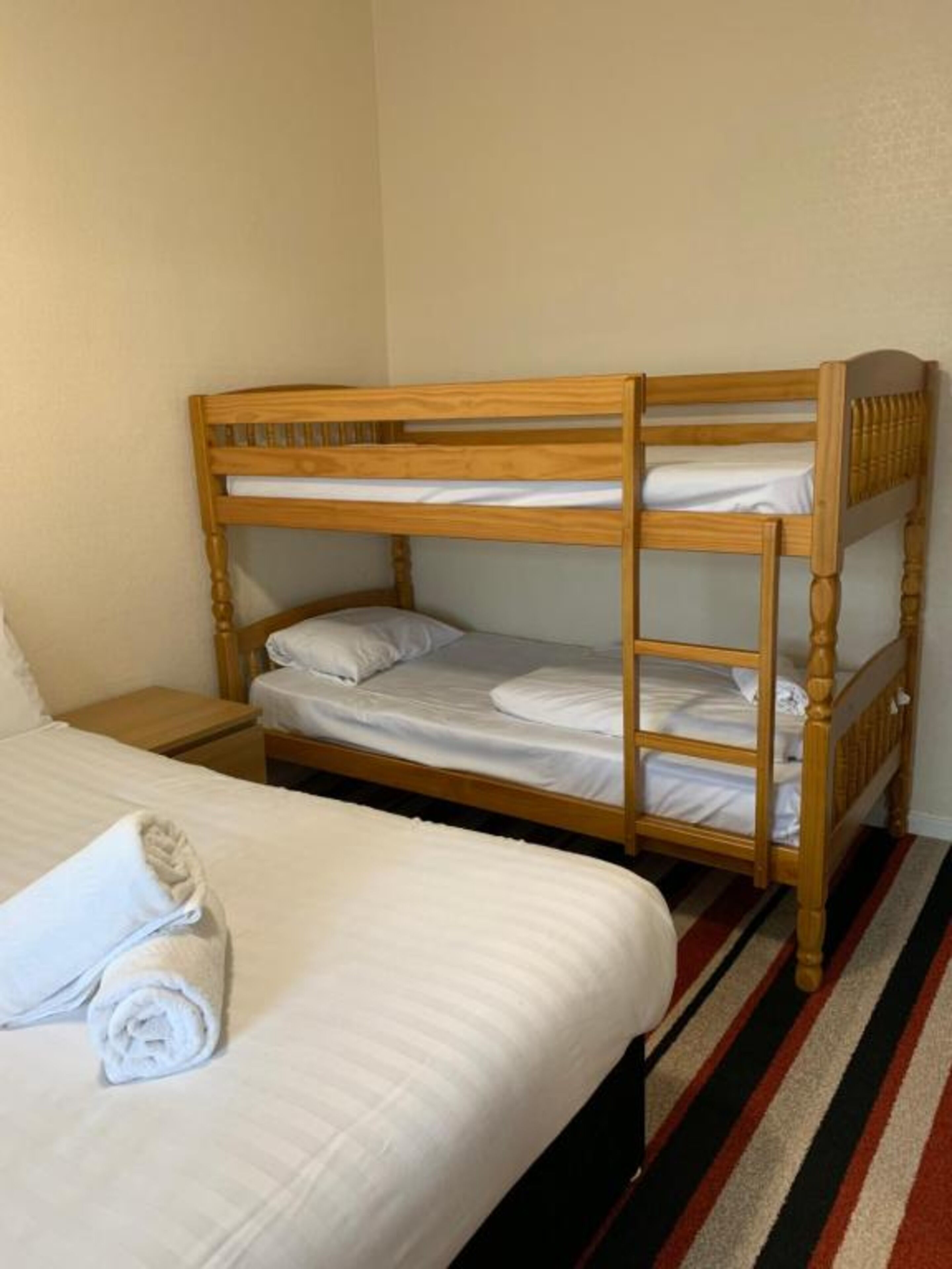 A bunk bed with two levels, a single bed with a rolled towel, and a striped rug.