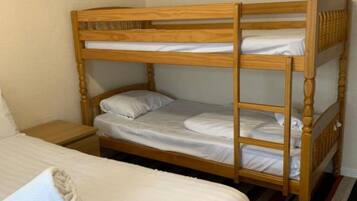A bunk bed with two levels, a single bed with a rolled towel, and a striped rug.
