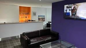 Un área de recepción con bar, sofá e imagen panorámica en una pantalla de televisión.