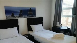 Habitación de hotel con dos camas, un cuadro de piedras apiladas, una mesita de noche con un control remoto y una ventana con cortinas.
