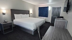 Ett hotellrum med en säng, sängbord, ett skrivbord, en stol, en tv och en dörr.