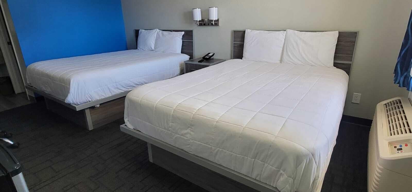 Una habitació d'hotel amb dos llits, una taula de nit amb un telèfon i una làmpada penjada a la paret.