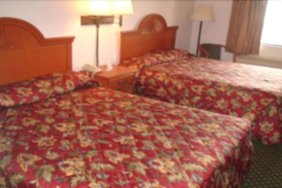 A hotel room with two beds, each with floral-patterned bedding. There is a nightstand with a lamp between the beds.