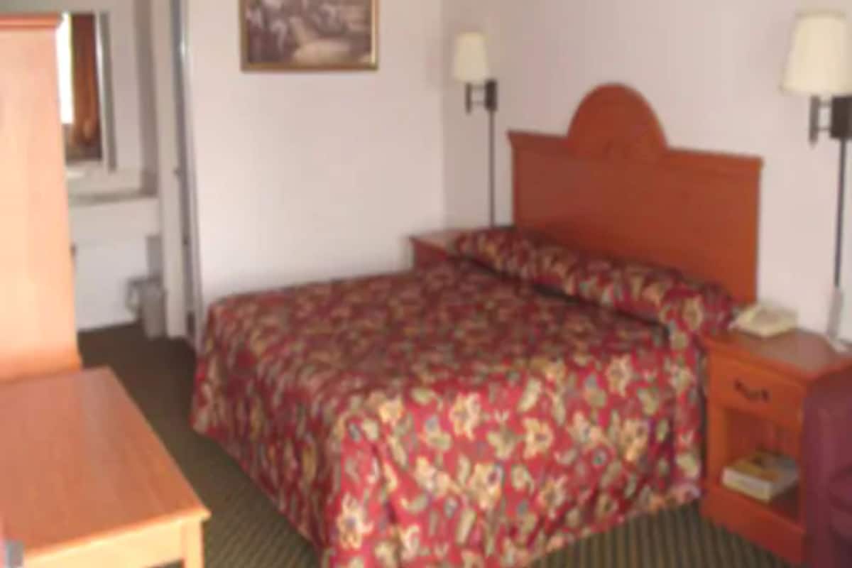A hotel room with a bed, a desk, and a nightstand with a lamp.
