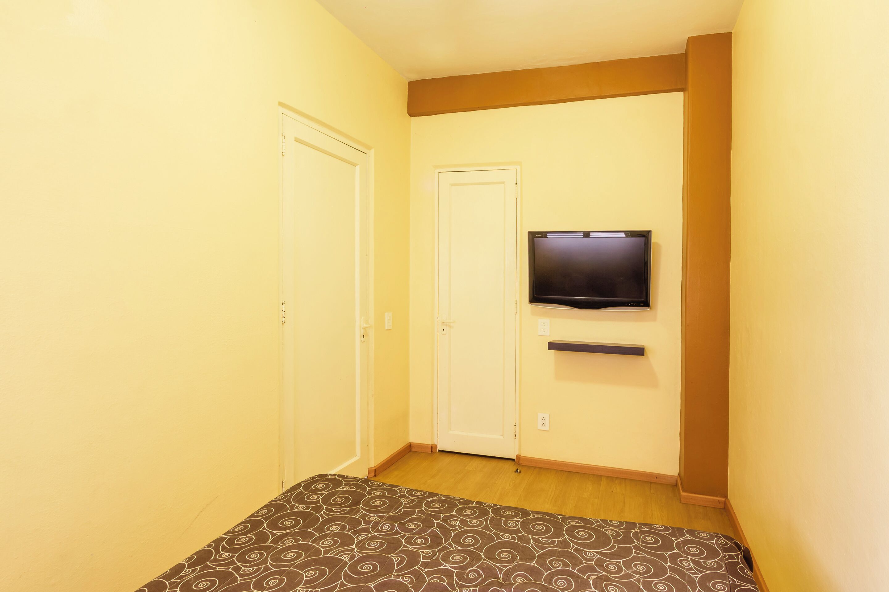 A small room with a bed, a television mounted on the wall, and a door.