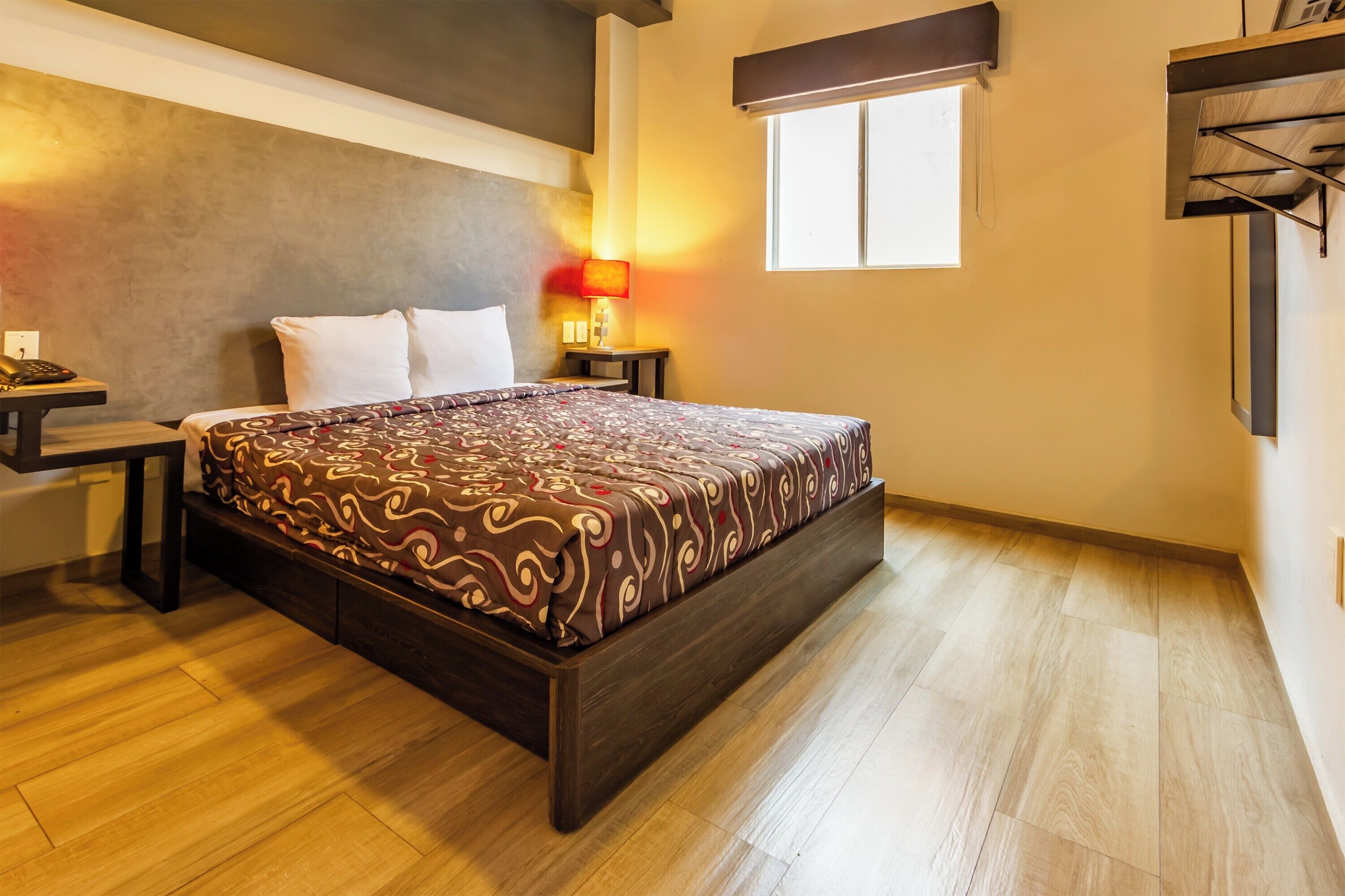 A bedroom with a bed, bedside tables, a lamp, a window, and a wall-mounted shelf.