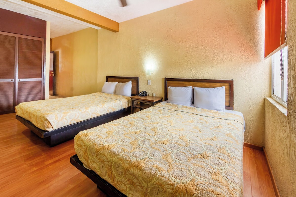 A hotel room with two beds, wooden flooring, a wardrobe, and a window with blinds.