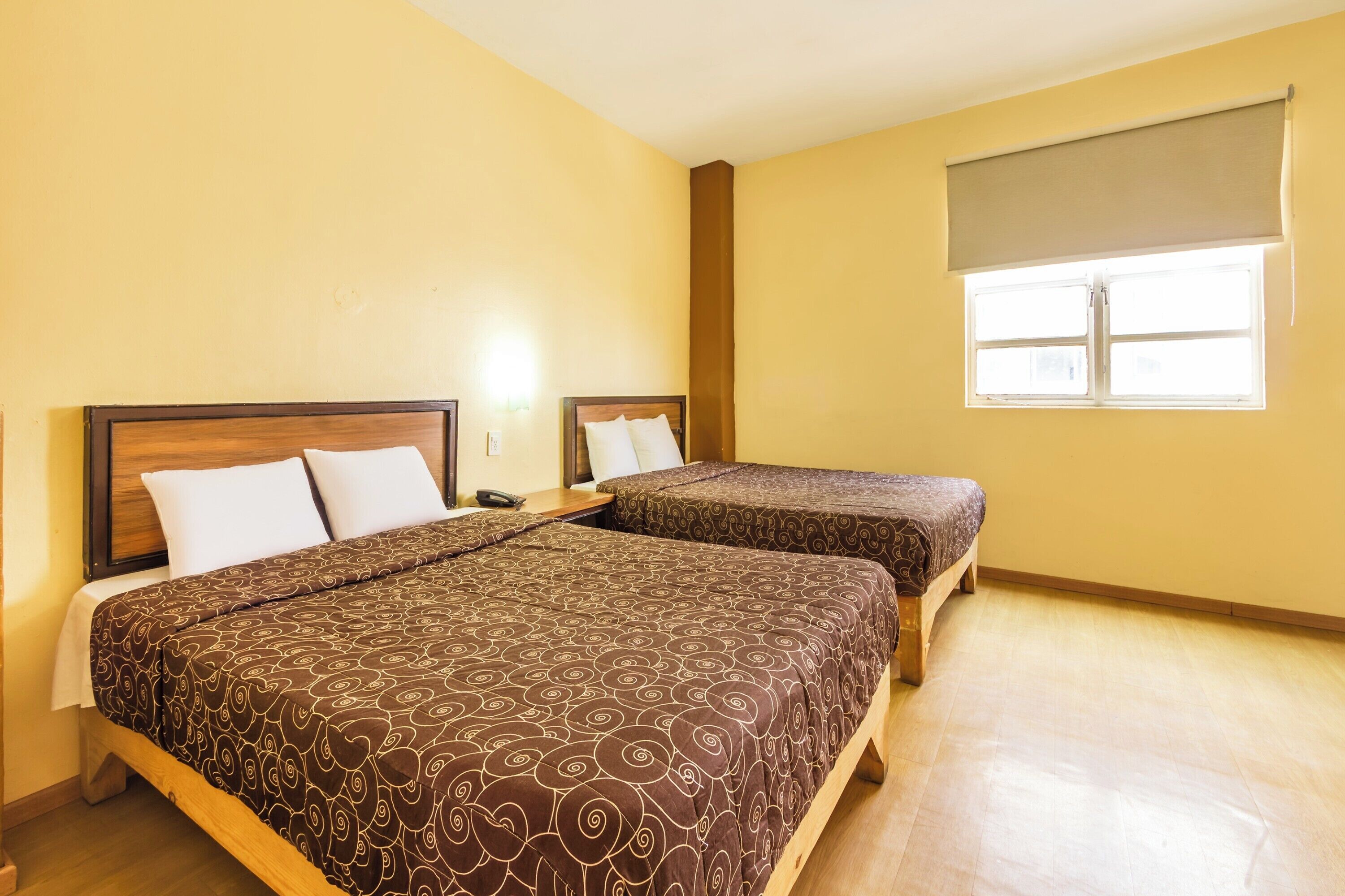 A hotel room with two beds, a window with a blind, and a wooden floor.