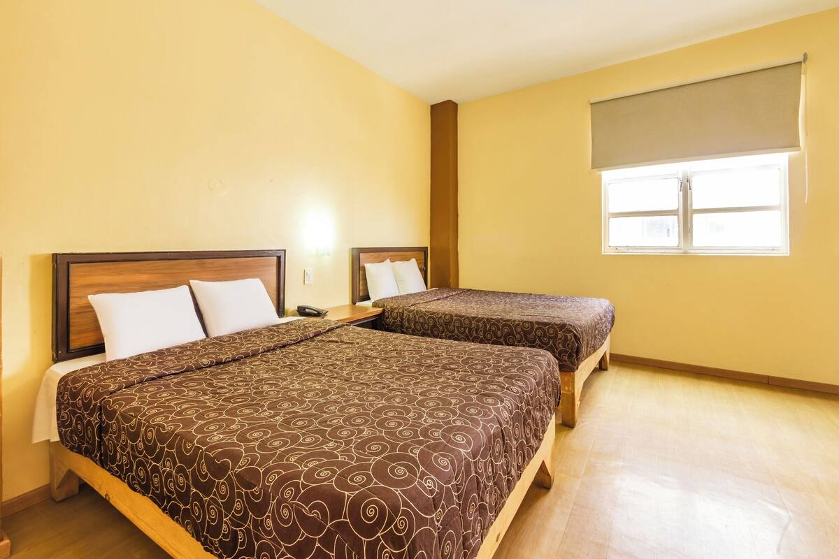 A hotel room with two beds, a window with a blind, and a wooden floor.