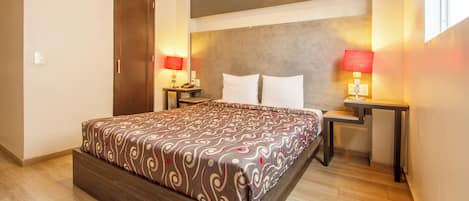 A hotel room with a large bed, two bedside tables with lamps, a wooden headboard, and a door.