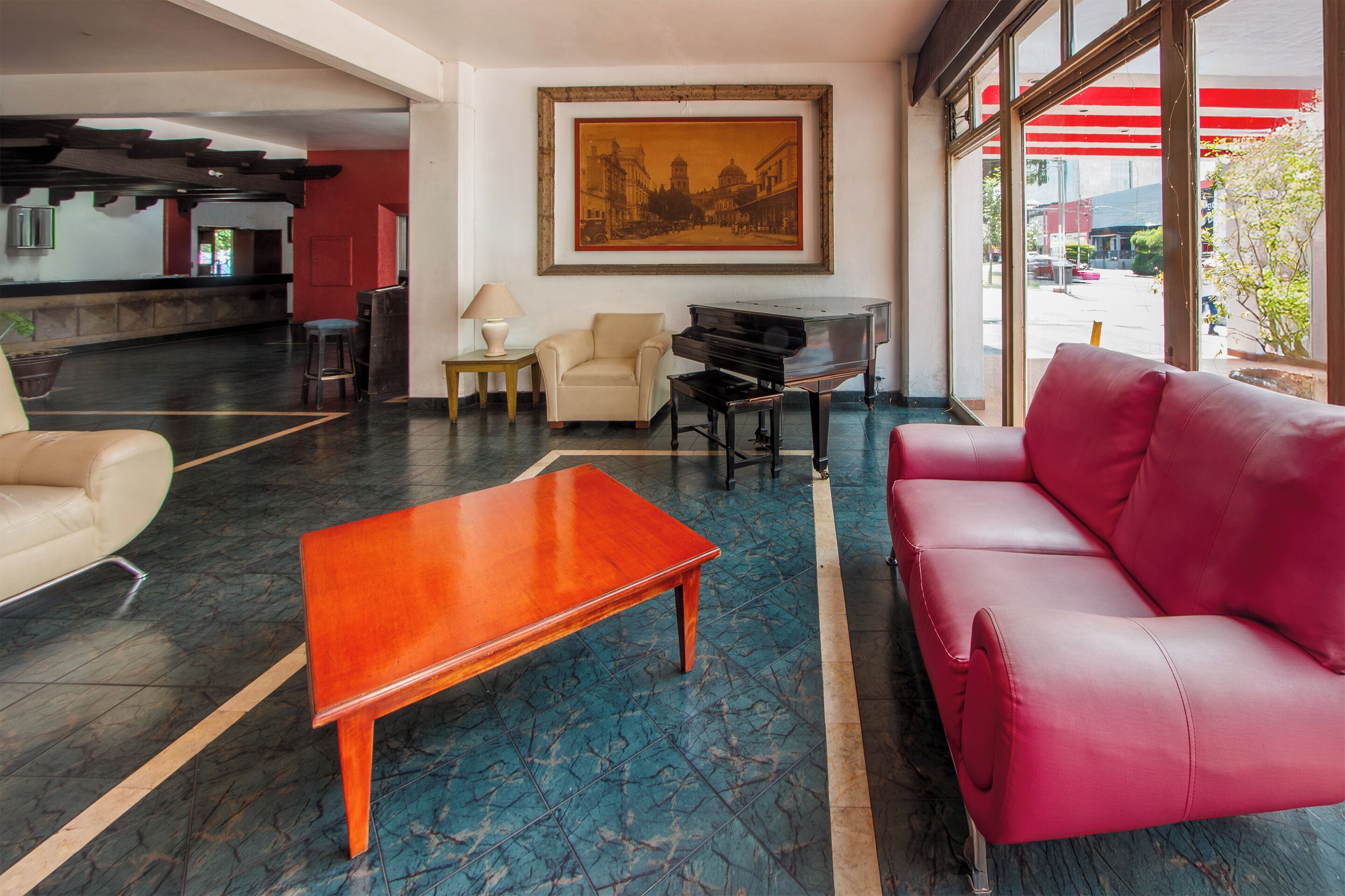 A lobby with a piano, a red sofa, a beige armchair, and a wooden coffee table.