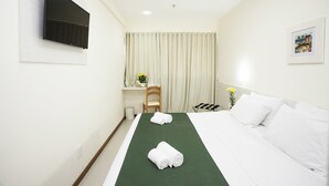 A hotel room with a bed, a desk, a chair, a TV, and a window with curtains. - Green Hotel Cabo Frio (Cabo Frio)
