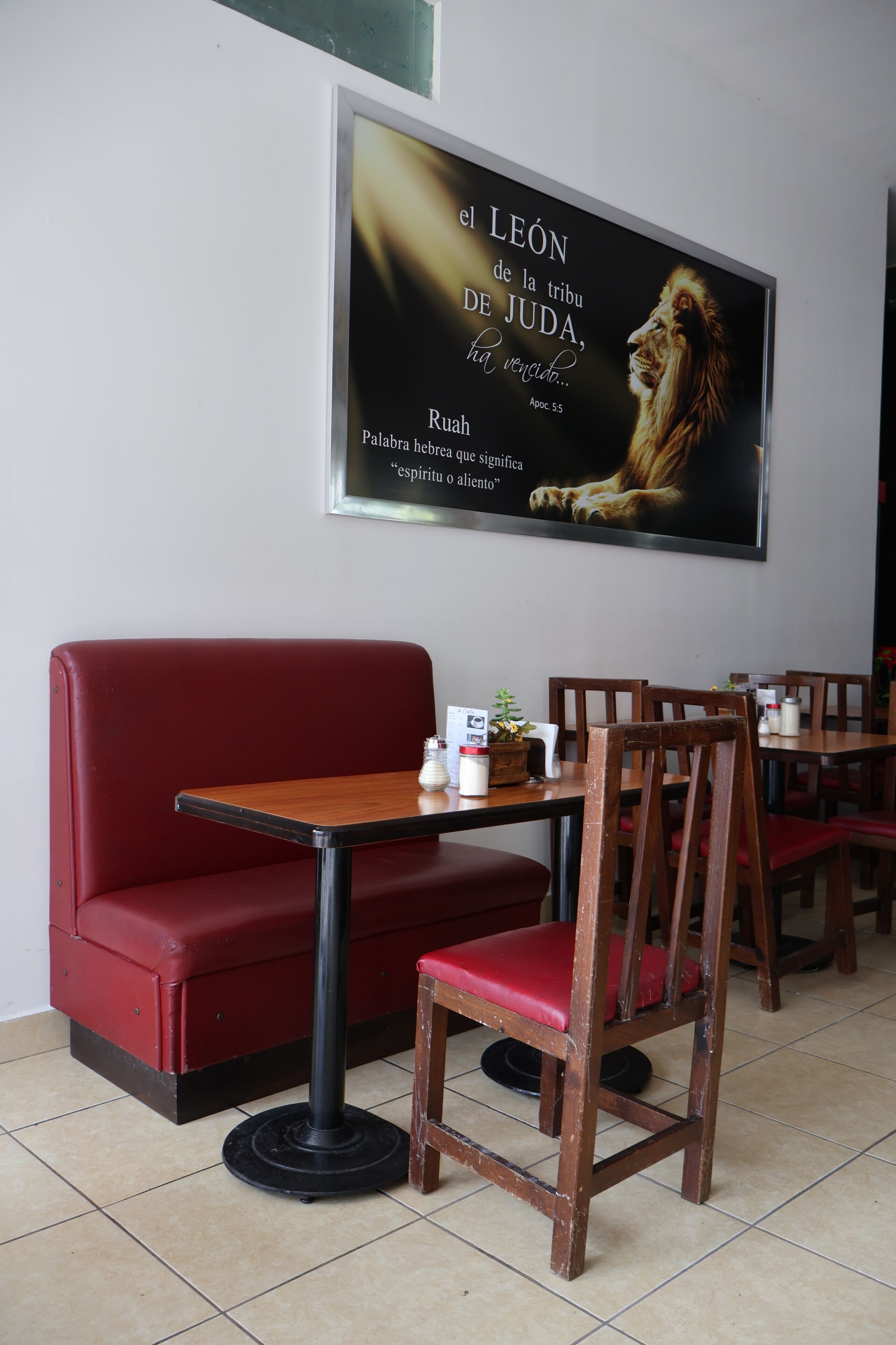 Een restaurantinterieur met een rode zithoek, houten stoelen en een tafel met een kleine plant en een menukaart.
