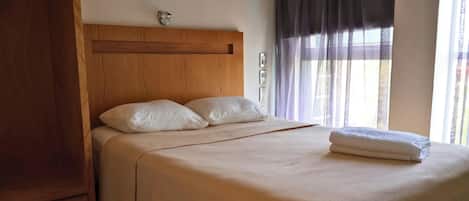 Un lit bien fait, avec une tête de lit en bois, des oreillers blancs et une serviette blanche pliée.