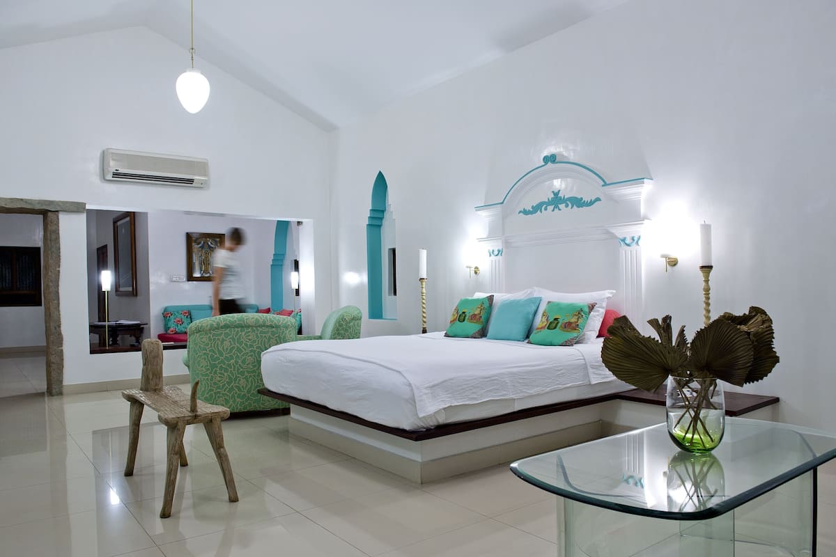 A modern bedroom with a bed, a glass table, a chair, and a vase with dried flowers.