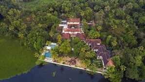 An aerial view of a tropical resort with a swimming pool, multiple buildings, and lush greenery surrounding the property. - Purity at Lake Vembanad (Cherthala)