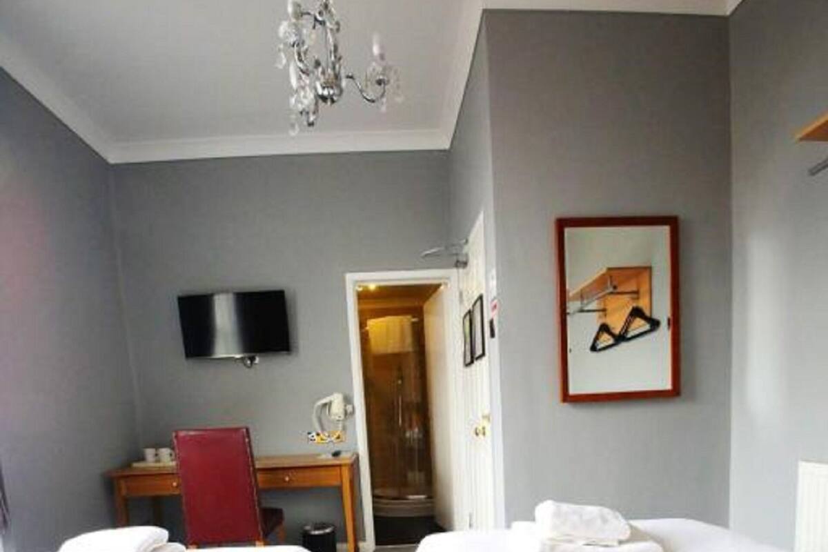 Hotellihuone, jossa on kaksi sänkyä, työpöytä, tuoli, televisio ja ovi, joka johtaa kylpyhuoneeseen.