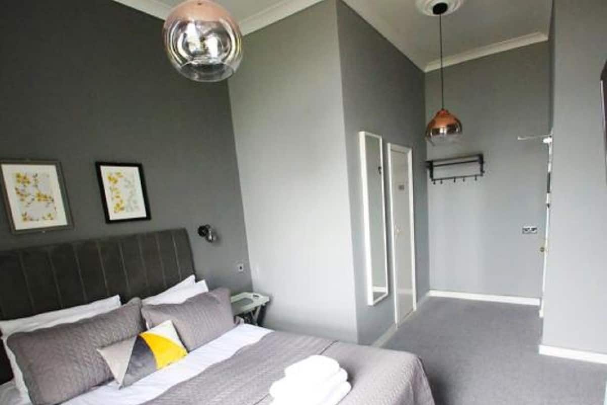 Moderni hotellihuone, jossa on suuri sänky, yöpöytä, peili ja vaatekaappi.