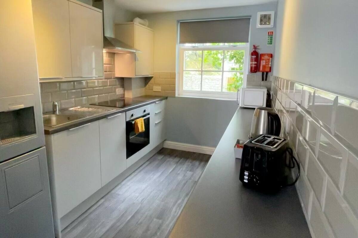 A compact kitchen with white cabinets, a built-in oven, a toaster, and a window providing natural light.