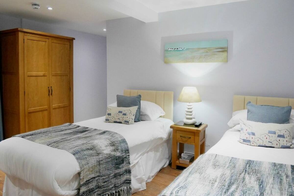 A hotel room with two beds, a wooden wardrobe, a bedside table with a lamp, and a painting on the wall.