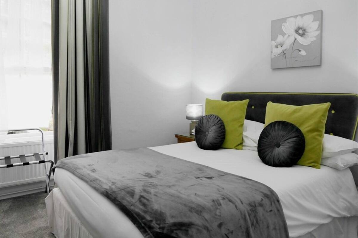 A hotel room with a bed, a nightstand, a lamp, and a window with curtains.