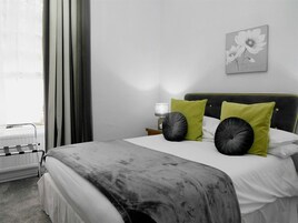 Quarto de hotel com cama, mesa de cabeceira, luminária e janela com cortinas.
