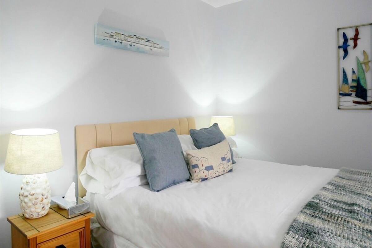 A neatly made bed with white and blue pillows, a bedside lamp, and a framed picture on the wall.
