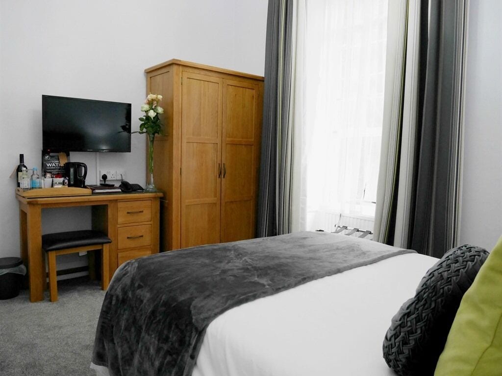 A hotel room with a bed, a desk with a television, a wardrobe, and a window with curtains.