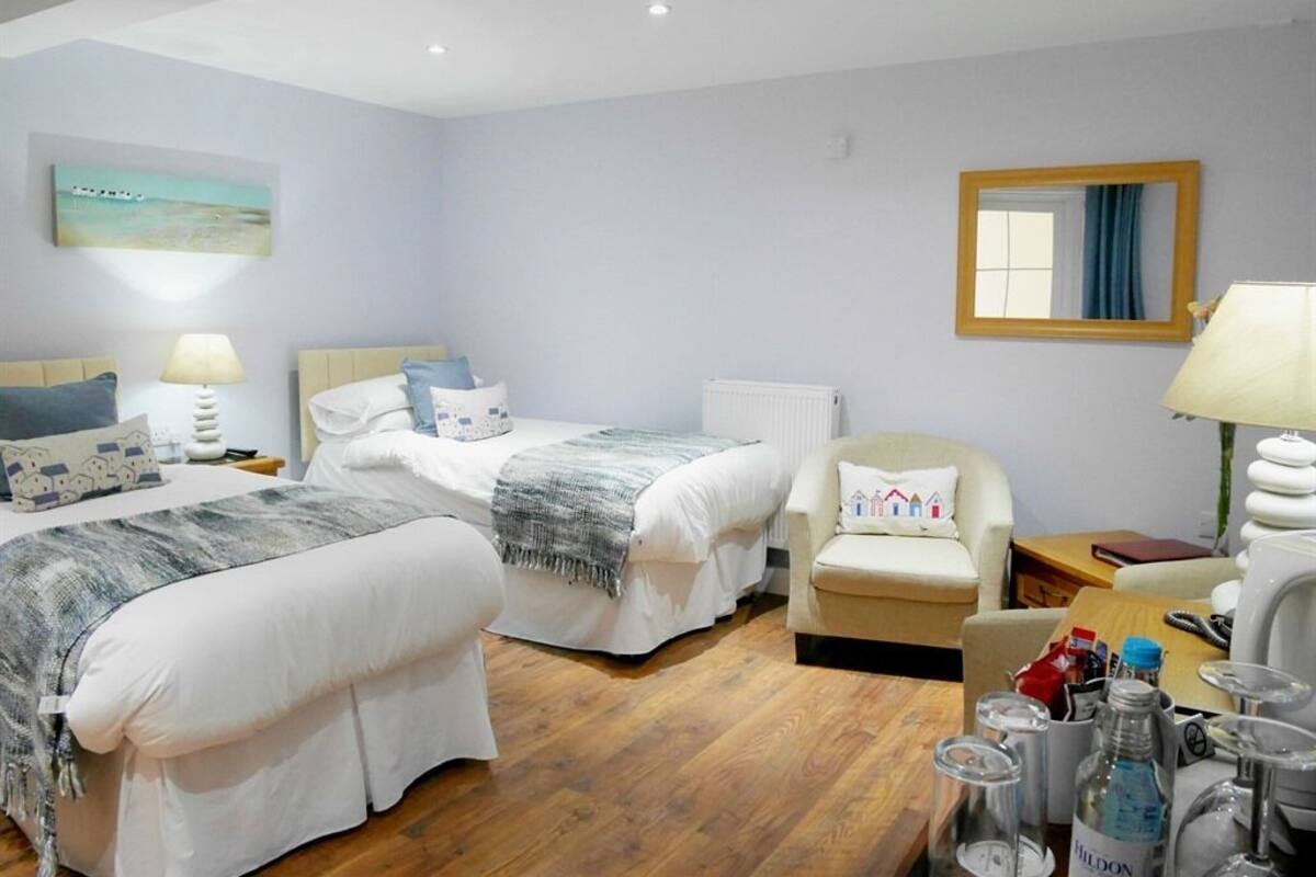 A hotel room with two beds, a chair, a table with a lamp, and a mirror on the wall.