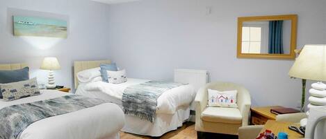 A hotel room with two beds, a chair, a table with a lamp, and a mirror on the wall.