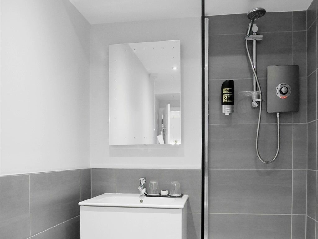 A modern bathroom with a white sink, a mirror, a shower with a handheld showerhead, and a control panel.