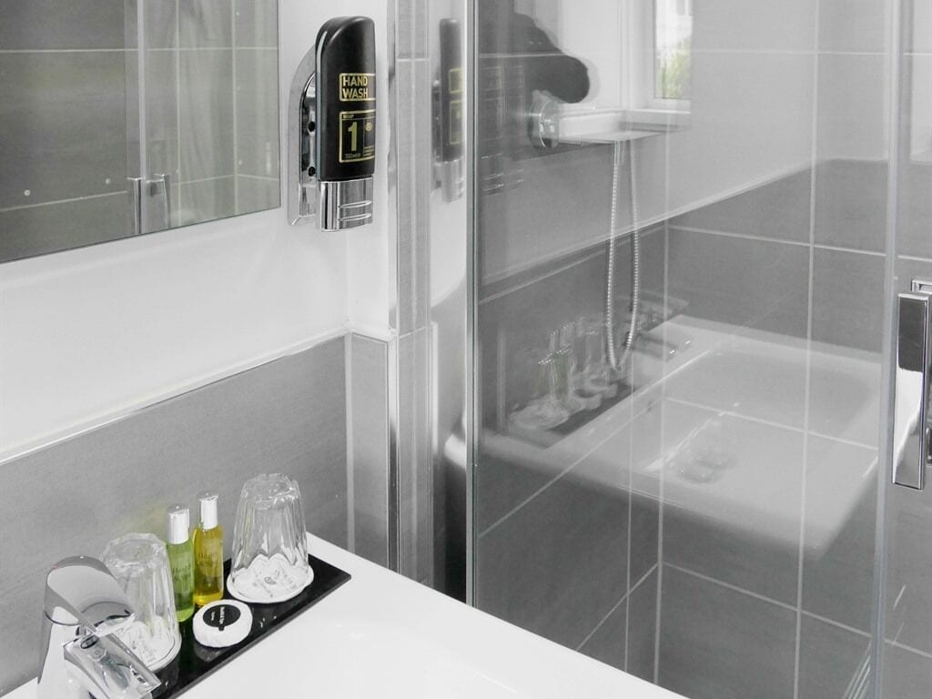 A modern bathroom with a glass shower enclosure, a handheld showerhead, and a variety of toiletries on a tray.