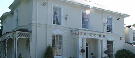 A two-story building with a symmetrical facade, large windows, and a central entrance with a decorative archway.