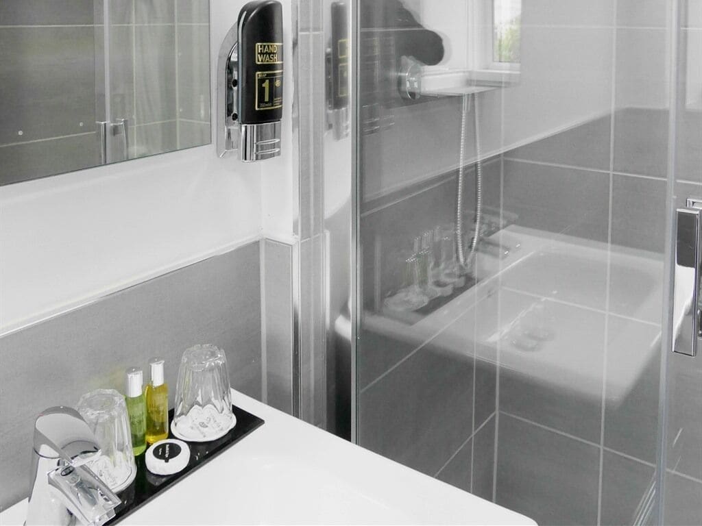 A modern bathroom with a glass shower enclosure, a white sink with toiletries, and a mirror.